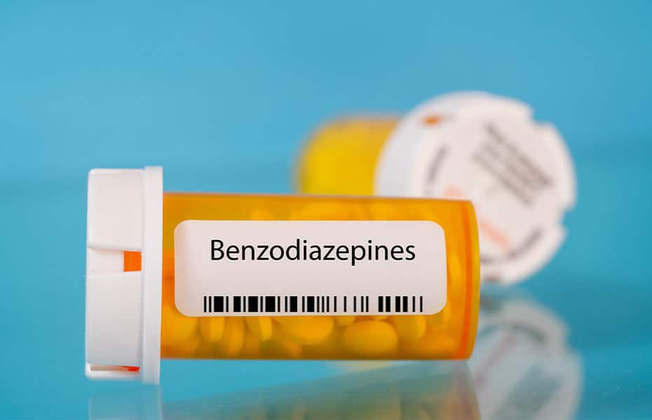 A bottle of benzodiazepine medication lying on its side on a blue background.