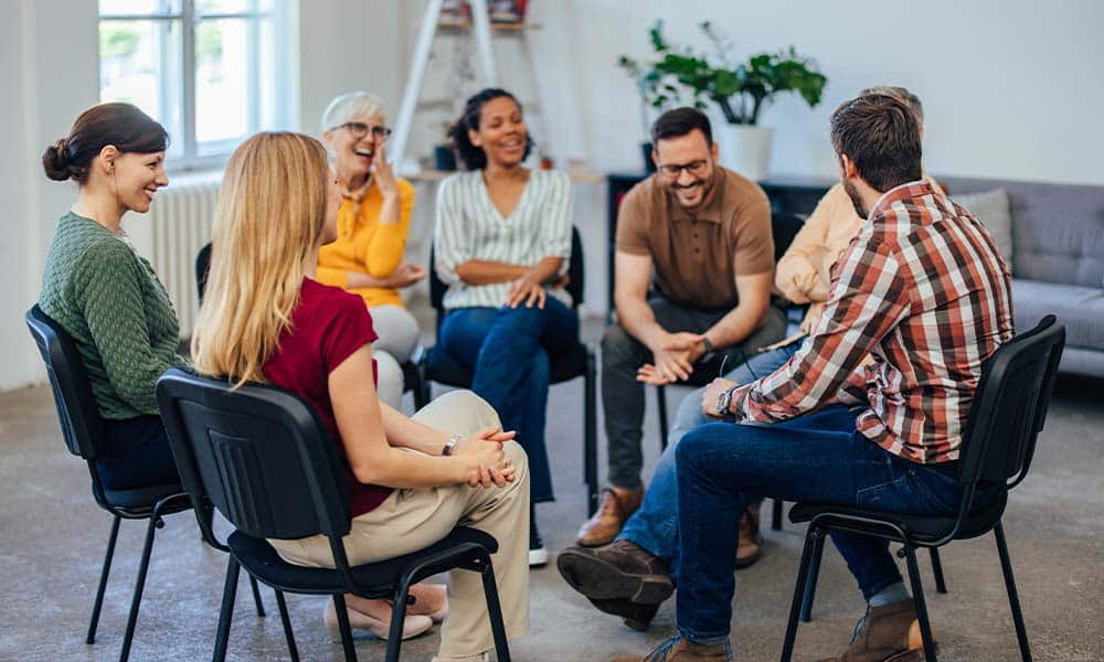 Coed group of drug rehab patients sitting in a circle during group therapy session in Hyde Park, MA.