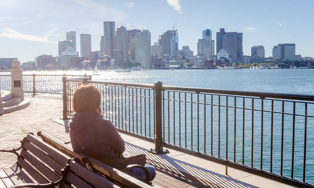 Woman sitting on a bench overlooking the Boston Harbor searching for drug and alcohol rehab. 