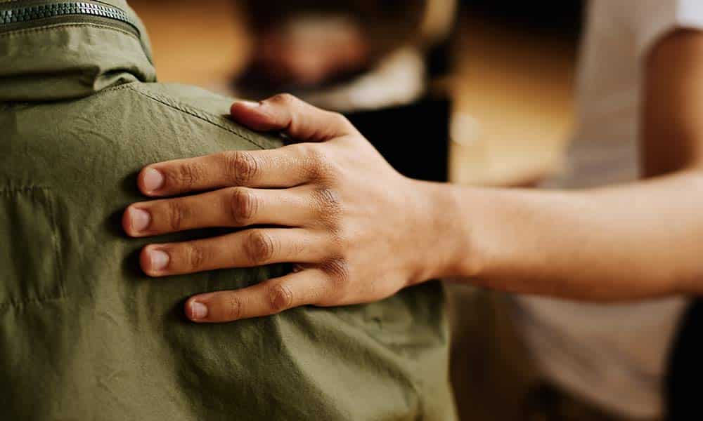 Veteran wearing a military jacket is comforted during TRICARE drug rehab.