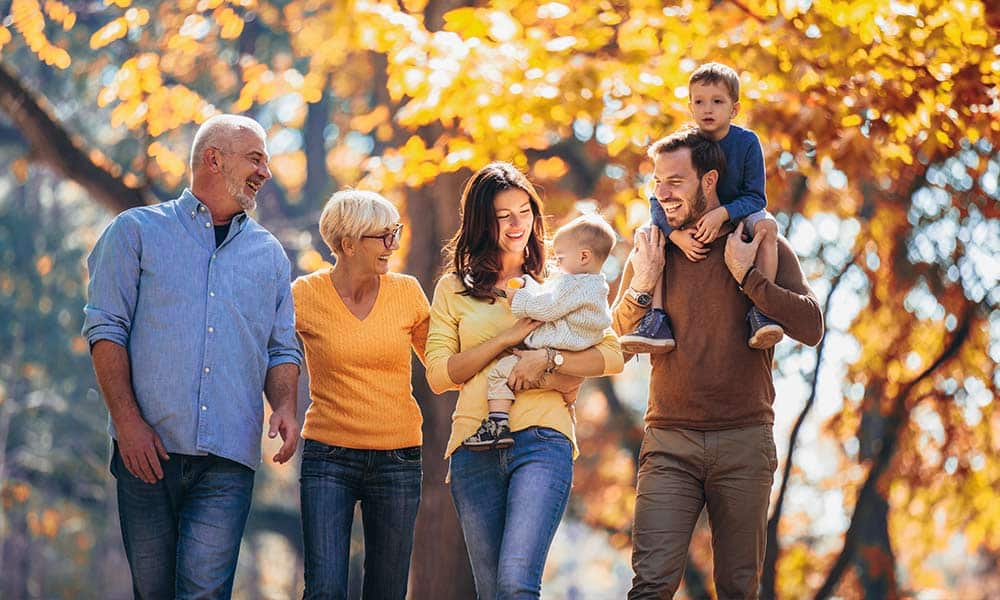 Happy, multigenerational family walking together outside symbolizing the happiness that can be experienced through family therapy.