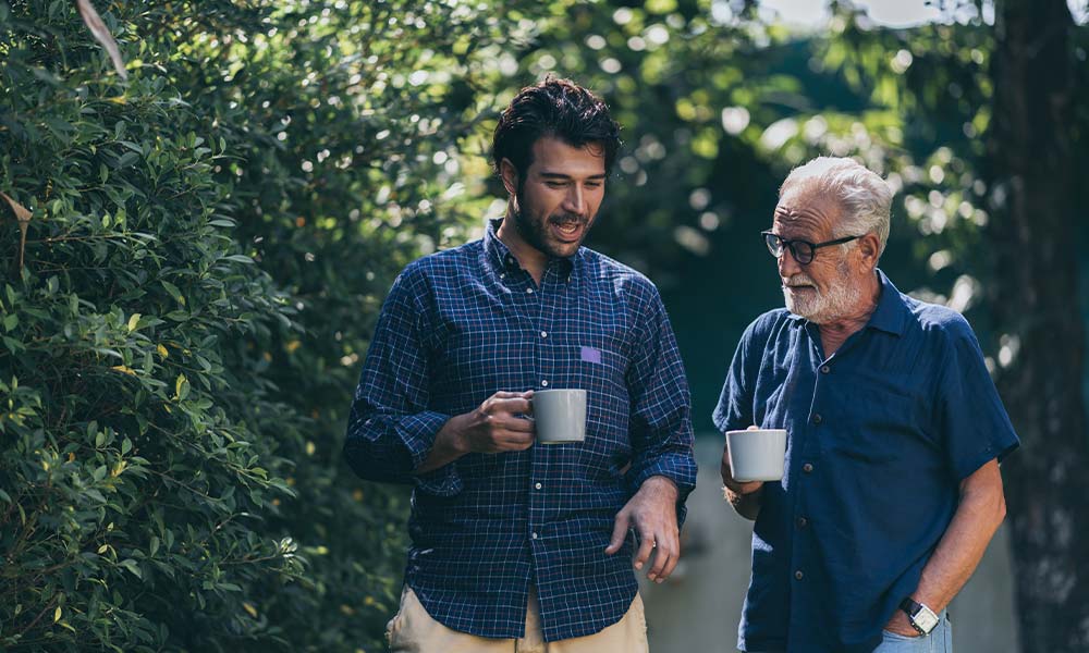 Father and son walking outside drinking coffee as they enjoy the benefits of relational therapy for addiction.