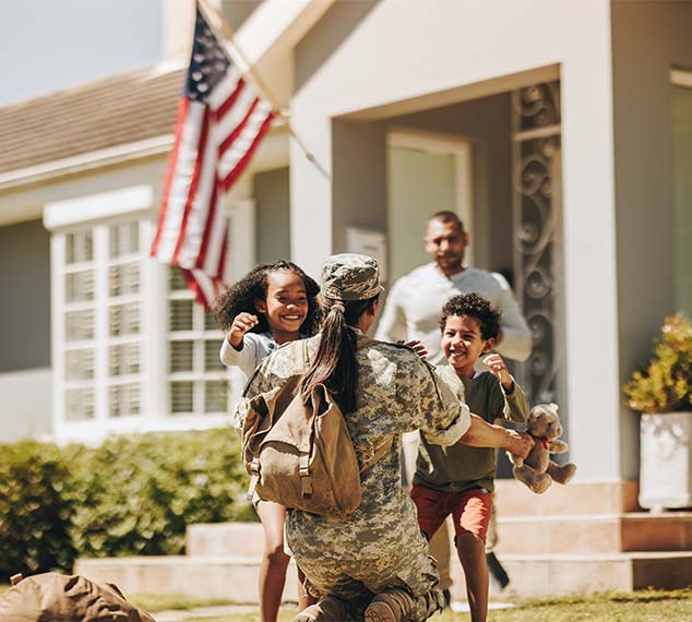 Female veteran greeting her family in their front yard with an american flag in the background