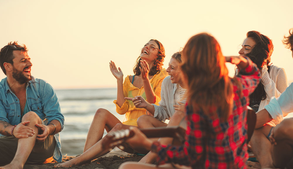 Friends sitting together on the beach at sunset, celebrating recovery and positive life changes.