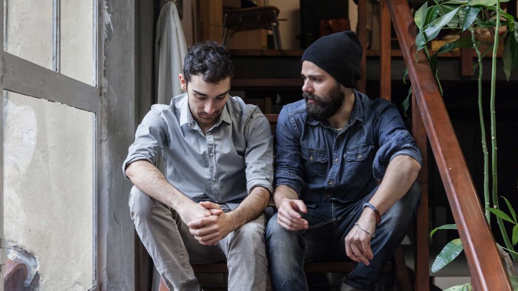 Two men sitting on stairs having a supportive, serious conversation about addiction and Section 35 involuntary commitment options in Massachusetts.